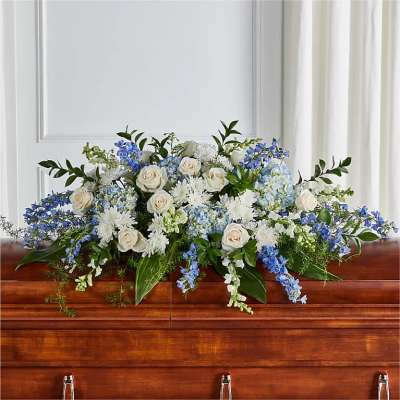 Long white and blue funeral spray of roses and mixed flowers on a wooden casket