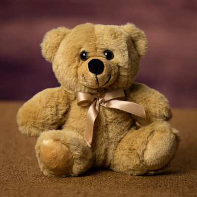 Soft tan teddy bear with a satin bow sitting on a brown surface