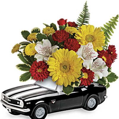 Bright yellow, red, and white flowers arranged in a black classic car-shaped ceramic container.