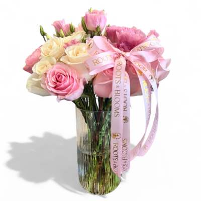 Pink and cream roses in a clear glass vase with a pink ribbon