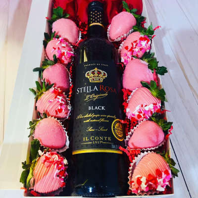 Wine bottle in a gift box surrounded by chocolate-covered strawberries and roses