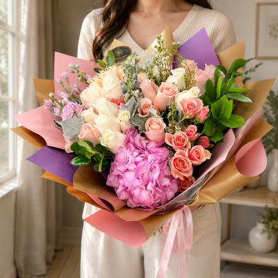 Large bouquet of pink, peach, and white roses with hydrangea in colorful wrap