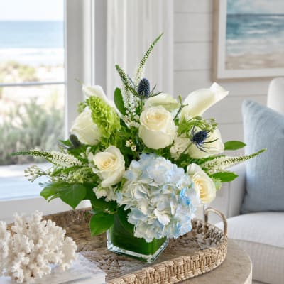 White roses and blue hydrangea in a glass vase with green accents