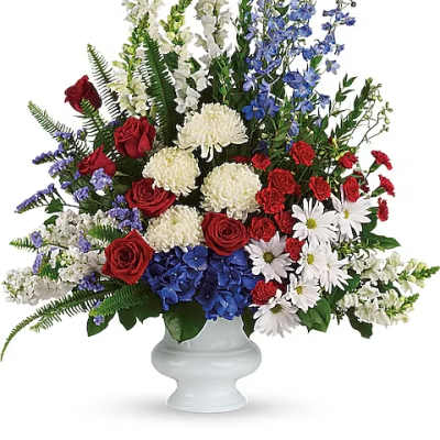Large mixed floral arrangement in a white urn vase with red, white, and blue flowers