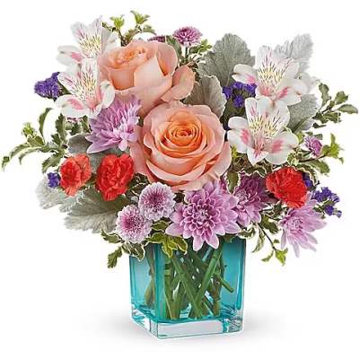 Mixed bouquet of peach roses, purple blooms, and white flowers in a blue glass vase