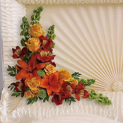 Floral arrangement with orange lilies, yellow roses, and red blooms on a white satin pillow