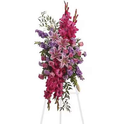 Tall floral spray with pink lilies, roses, and purple flowers on a white stand
