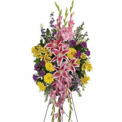 Standing floral spray with pink lilies, yellow daisies, and purple flowers on an easel