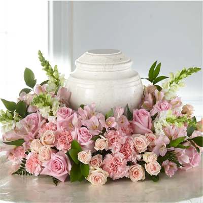 Pink roses and carnations arranged around a white urn.