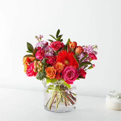 Bright mixed bouquet of pink, orange, and red flowers in a short clear glass vase