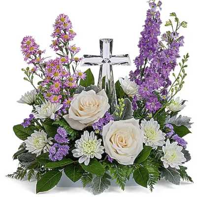 White roses and purple flowers arranged around a silver cross.
