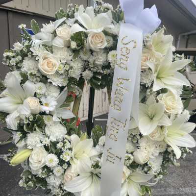 White floral funeral wreath with lilies, roses, and a memorial ribbon