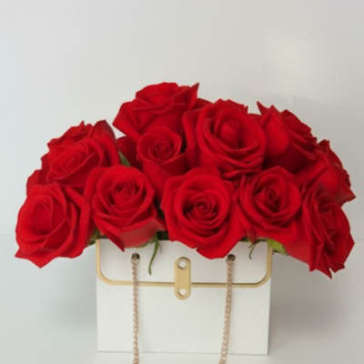 Red roses arranged in a white handbag-style box with a gold chain