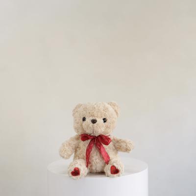 Plush teddy bear with a red ribbon sitting on a white pedestal