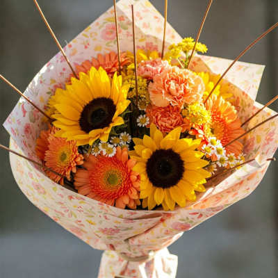 Bouquet of sunflowers, orange gerberas, and carnations in floral wrap