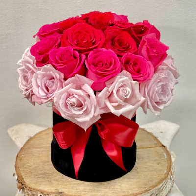 Pink and red roses arranged in a black hat box with a red ribbon