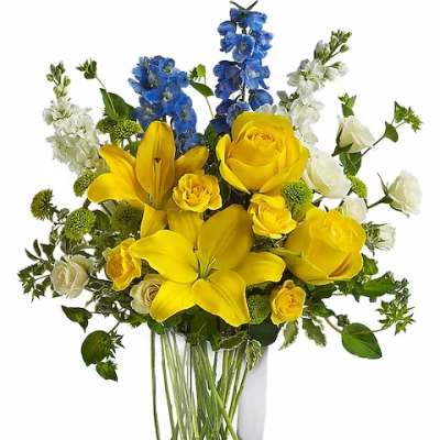 Yellow lilies and roses in a clear glass vase with blue and white flowers