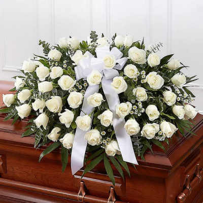 White rose funeral spray with a white ribbon on a casket