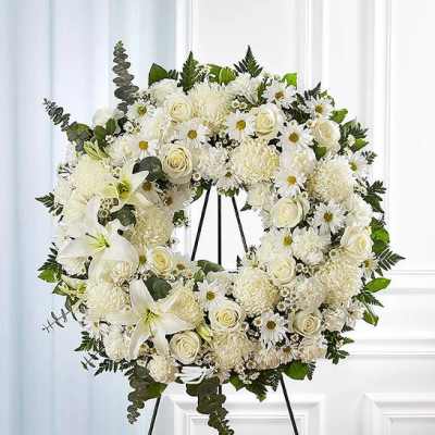 White floral wreath on a black stand with roses and daisies