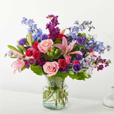 Mixed bouquet of pink, purple, and blue flowers in a glass vase