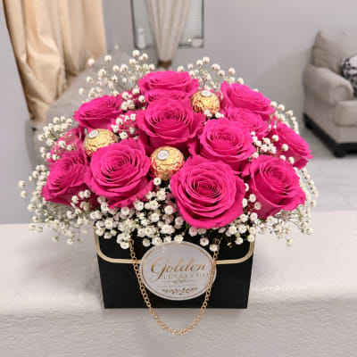 Hot pink roses in a black gift box with white filler flowers and gold chocolates