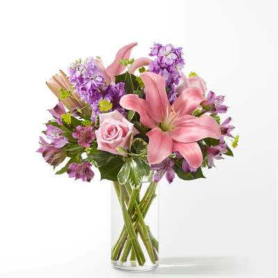 Pink lilies and roses in a clear glass vase with purple flowers