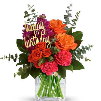 Bouquet of orange and pink flowers in a clear vase with a happy birthday sign