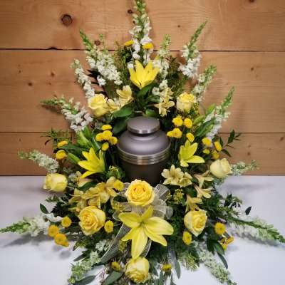 Yellow and white funeral floral spray around a metal urn