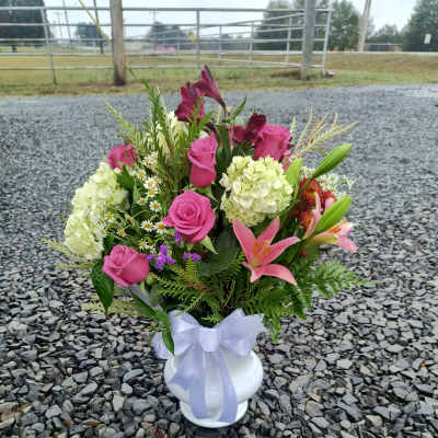 Pink roses and lilies arranged in a white vase with a lavender ribbon