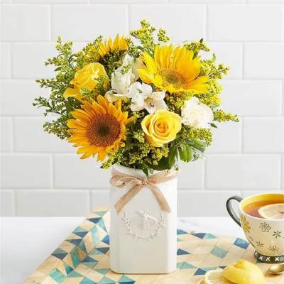Yellow sunflowers and roses arranged in a white vase with a ribbon