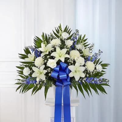 White lilies and blue flowers in a standing arrangement with a blue ribbon