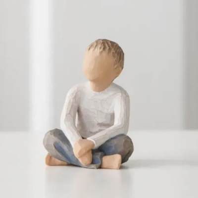 Small carved figurine of a seated child in a white shirt and blue pants