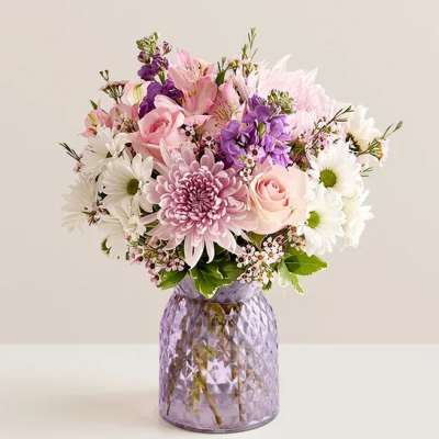 Pastel bouquet of pink roses, mums, daisies and purple blooms in a lavender glass vase