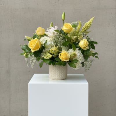 Yellow roses and white blooms arranged in a cream vase
