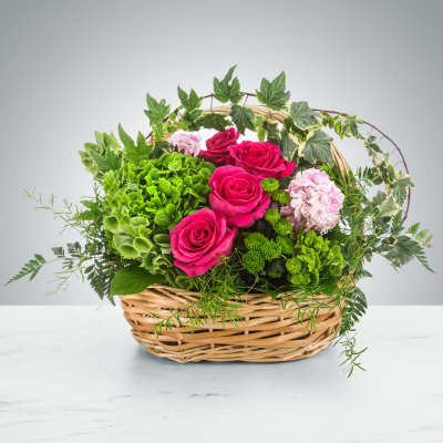 Basket arrangement of pink roses, green hydrangea, and pale pink blooms