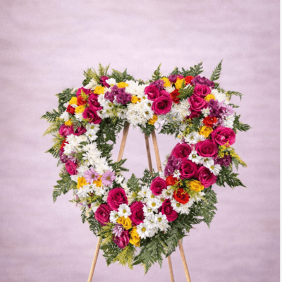 Heart-shaped standing wreath with pink and yellow roses and white daisies on a wooden easel