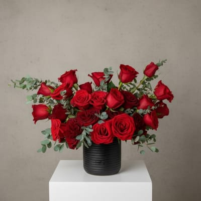 Red roses arranged in a black vase with eucalyptus accents