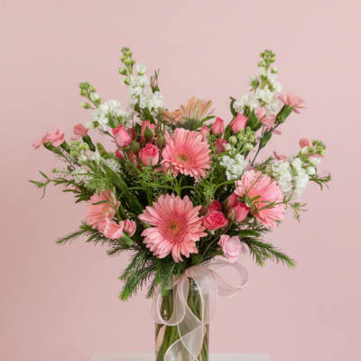 Pink mixed flower bouquet in a clear glass vase with a sheer ribbon