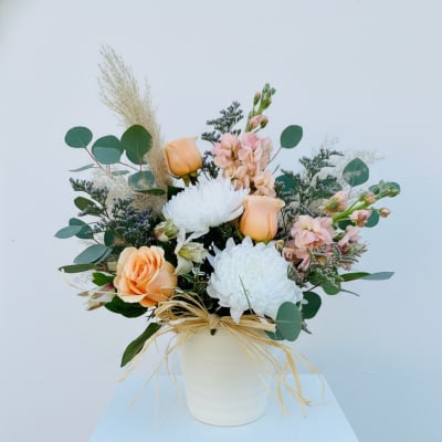 Peach and white floral arrangement in a white vase with eucalyptus