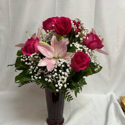 Pink roses and a pale lily arranged in a tall vase
