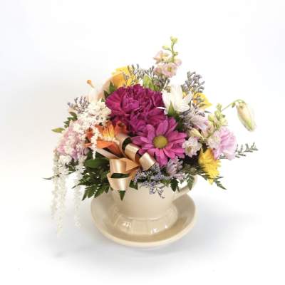 Colorful mixed flower arrangement in a cream teacup and saucer