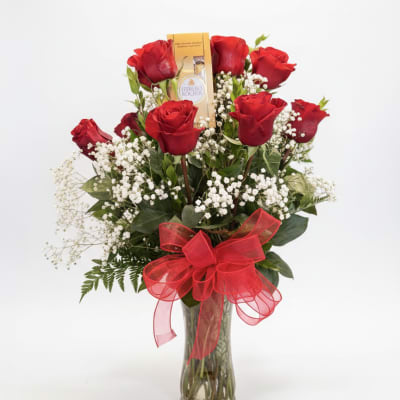Red roses in a clear glass vase with a red bow and a chocolate box