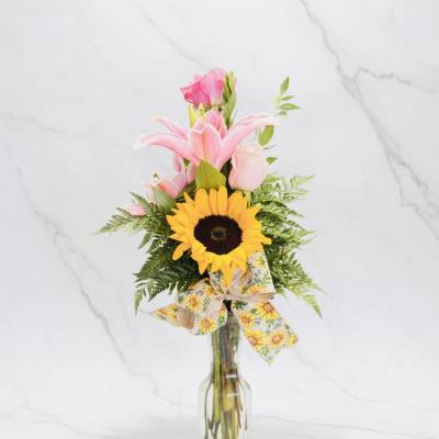 Pink lilies and a sunflower in a clear glass vase with a ribbon