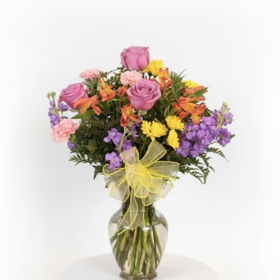 Mixed bouquet of pink roses, purple flowers, and yellow blooms in a glass vase