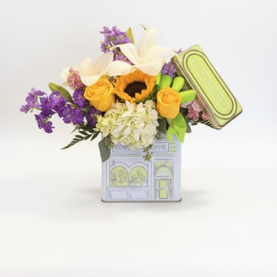 Bouquet of yellow roses, white lilies, and purple flowers in a decorative tin