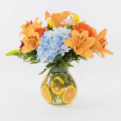 Orange lilies and blue hydrangeas in a glass vase with sliced oranges