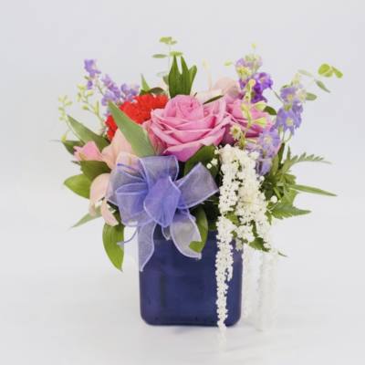 Pink and purple mixed bouquet in a blue vase with a lavender ribbon