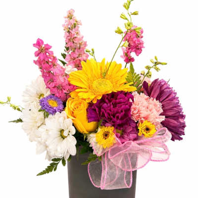 Colorful mixed bouquet in a dark square vase with a pink ribbon