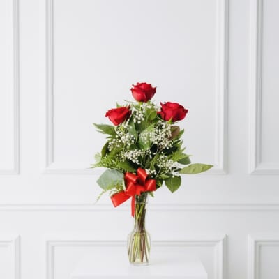 Red roses in a clear glass vase with a red ribbon