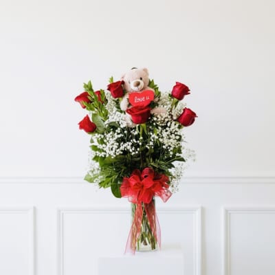 Red roses in a glass vase with a teddy bear and heart topper